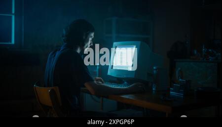 Caucasian Male Web Designer Using Old Desktop Computer In Retro Garage Late At Night. Focused Internet Enthusiast Writing Code At Home. Programming Successful Online Forum Website In Nineties. Stock Photo