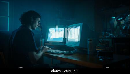 Caucasian Male Programmer Using Old Desktop Computer With Two Monitors In Retro Garage Late At Night. Evil Hacker Searching For Software Vulnerabilities, Coding DDOS Attack, Trojan Horse Program. Stock Photo