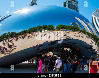 Chicago, Illinois, USA - 18 July 2024: A large, shiny, reflective sculpture, known as Cloud Gate, is viewed from underneath, with visitors gathering a Stock Photo