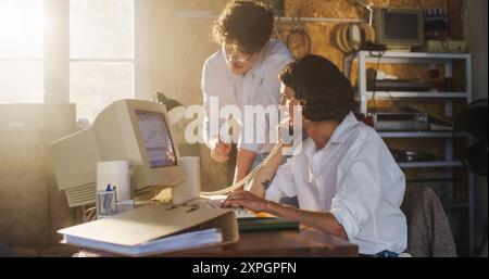 Two Caucasian Male Stock Brokers Working In Retro Garage, Using Old Desktop Computer With Candlestick Chart And Landline Phone To Pitch A Public Company To Investor. Partners Trading On Stock Exchange Stock Photo