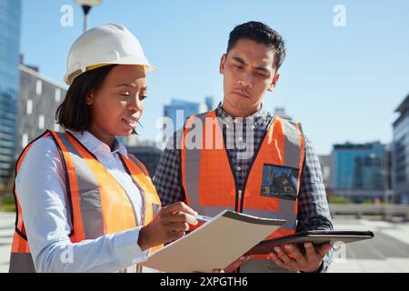 Diverse Construction Workers Reviewing Plans at an Urban Construction Site Stock Photo
