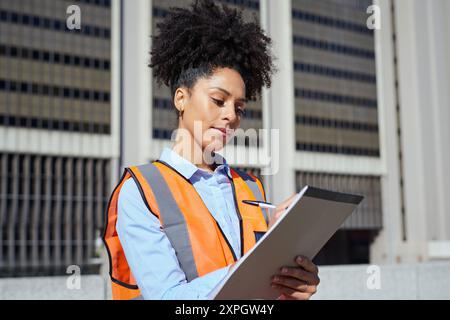 Female Engineer in Safety Vest Inspecting Construction Site with Clipboard Stock Photo