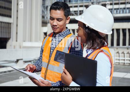 Diverse Engineers Discussing Blueprint Plans at Construction Site Stock Photo