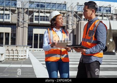 Diverse Engineers Discussing Project Outdoors at Modern Construction Site Stock Photo