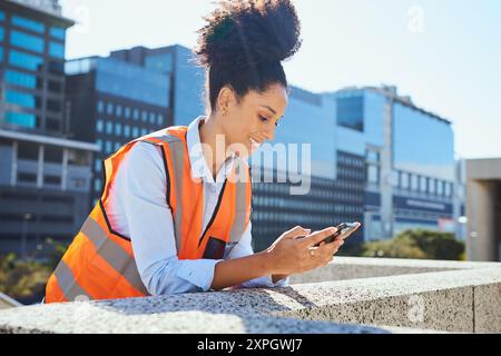 Young Female Engineer Using Smartphone Outdoors in Urban City with Office Buildings Stock Photo