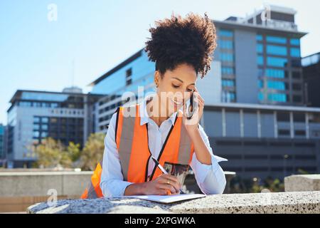 Female Engineer Talking on Phone and Taking Notes At Construction Site Stock Photo