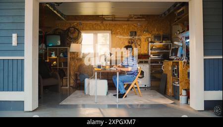 Caucasian Male Software Engineer Entering Retro Garage And Sitting At His Work Desk With Old Desktop Computer. Focused Man Starting Software Startup Company In Nineties, Working On Digital Product. Stock Photo