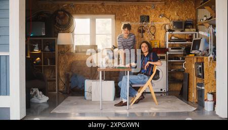 Two Caucasian Male Tech Startup Founders Using Old Desktop Computer In Retro Garage, Looking At Camera And Smiling. Programmer And UX Designer Starting Internet Business In Nineties. Nostalgia Concept Stock Photo