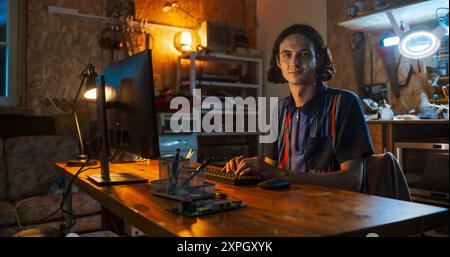 Portrait of Caucasian Male Software Engineer Programming On Desktop Computer In Home Garage, Looking At Camera And Smiling. Ambitious Man Working Innovative Online Service Startup Company at Night. Stock Photo