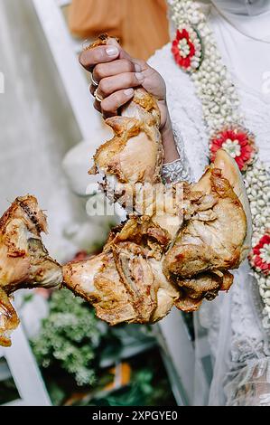 the bride raises a grilled chicken after winning more than the groom in the traditional Javanese traditional pulling of the bakakak chicken at a weddi Stock Photo