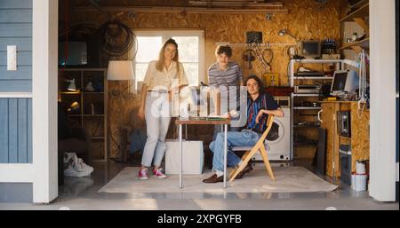 Diverse Team Of Three Young Startup Company Founders In Retro Garage With Old Desktop Computer. Male And Female Entrepreneurs Looking At Camera And Smiling, Developing Online Service In Nineties. Stock Photo