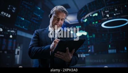 Low Angle Portrait of a Successful Stock Exchange Manager Working in Modern Office. Proactive Trader Browsing Internet on a Tablet Computer, Using Software with Stock Market Auction Operators Stock Photo