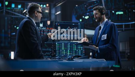 Two Successful Traders Analyzing Real-Time Financial Data and Reports About the State of the Finance Market. Stock Exchange Professionals Discussing Buy and Sell Options For Different Bonds Stock Photo