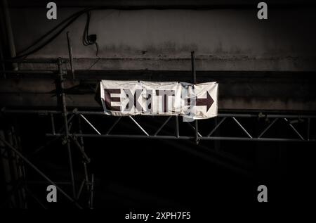 Exit sign with an arrow on a weathered white banner among a dark industrial site Stock Photo