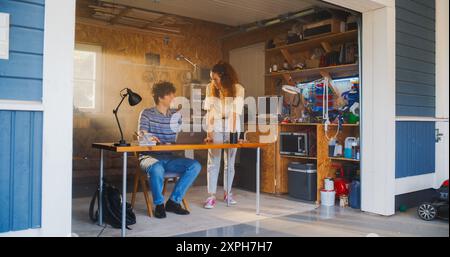 Caucasian Male Software Developer And Hispanic Female User Interface Designer Talking And Using Laptop Computer in Garage At Home. Diverse Young Startup Founders Working On Innovative Online Service. Stock Photo