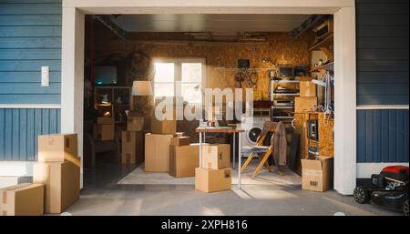 Establishing Shot Of Small Business Owners Empty Workplace With Laptop In Garage. Cardboard Boxes With Products Packed For Shipping to Clients Laying Around. Family Business, Entrepreneurship Concept. Stock Photo