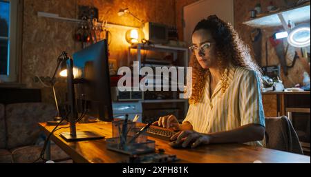 Hispanic Female Software Engineer Programming on Desktop Computer In Retro Garage Late At Night. Ambitious Woman Starting Technological Startup Company. Coding Innovative Online Service At Home. Stock Photo