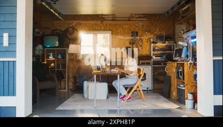 Hispanic Female Software Developer Programming On Old Desktop Computer In Retro Garage With Random Appliances. Woman Working On Innovative Online Service Startup Company In Nineties. Nostalgia Concept Stock Photo
