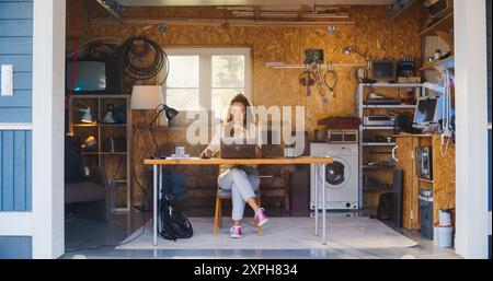 Hispanic Female Programmer Coding On Laptop Computer In Garage At Home. Young Woman Working On Innovative Software As A Service Startup For Business. Digital Entrepreneur Starting Company Concept. Stock Photo