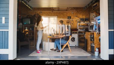Diverse Team Of Three Young Tech Startup Company Founders Working In Retro Garage, Using Old Desktop Computer. Male And Female Entrepreneurs Developing Innovative Online Service In Nostalgic Nineties. Stock Photo