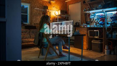 Hispanic Female Programmer Writing Code On Desktop Computer In Garage At Home. Woman Working On Innovative Software As A Service Startup For Business At Night. Digital Entrepreneur Starting Company. Stock Photo