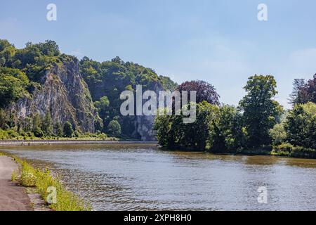 Meuse river with abundant water against rocky mountain with wild vegetation on blurred fog background, trees with green foliage, sunny summer day in N Stock Photo