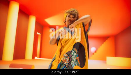 Beautiful Black Woman in African Outfit Dancing Energetically in Geometric Abstract Orange Environment. Creative Female Performing Dance Choreography in Bright Studio, Making Moves, Practicing. Stock Photo