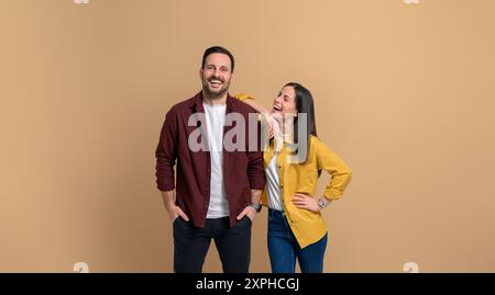 Beautiful woman with hand on boyfriend's shoulder looking at him and laughing. Charming young couple posing cheerfully while standing together against Stock Photo