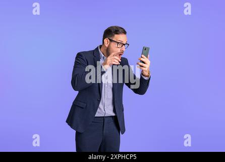 Displeased young businessman dressed in formal wear reading e-mails on mobile phone. Worried male professional entrepreneur using cellphone while stan Stock Photo