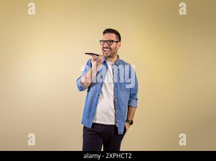 Cheerful handsome male freelancer with hand in pocket talking over speaker on smart phone. Happy young businessman sending voice mail through cellphon Stock Photo