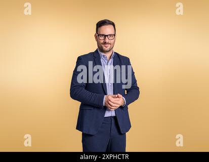 Portrait of young businessman wearing glasses and elegant blue suit clasping his hands. Male professional posing confidently while standing isolated o Stock Photo
