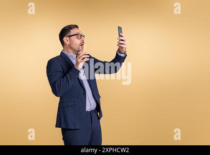 Shocked young business manager with mouth open reading bad news over smart phone. Stressed out entrepreneur checking e-mails over cellphone while stan Stock Photo