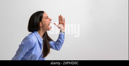 Side view of successful female professional screaming and gesturing in joy while standing isolated on background. Young businesswoman dressed in casua Stock Photo