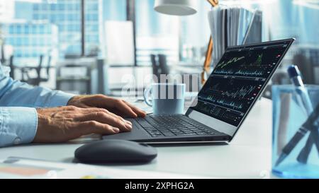 Close-Up On Hands Of Professional Broker Using Laptop Computer With Stock Options Graphs And Charts On Screen. Man Analyzing Stock Market Data And Enjoying Coffee In Hedge Fund Office. Stock Photo