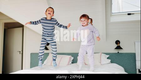 Children, jump and playing on bed in home for fun activity, entertainment and energy in morning with smile. Sibling love, people and playful with Stock Photo