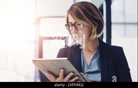 Business woman, research and reading with tablet for news, data or study on corporate development at office. Young female person or employee with Stock Photo