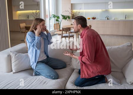 Married couple quarreling fighting shouting yelling at each other sitting on sofa in living room. Stock Photo