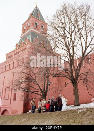 A wedding party strolls along the exterior walls of the Kremlin in Moscow on a chilly day in April 2006. The group includes the bride and groom, family members, and friends all dressed warmly. Stock Photo