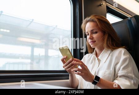 Modern tech-savvy businesswoman messaging online with her smartphone while traveling for work by train. Work on the go. Stock Photo