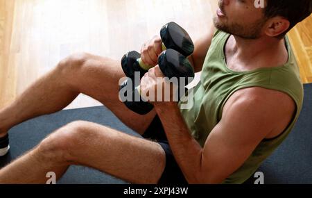 man sitting on floor doing abdominal exercise using dumbbells Stock Photo