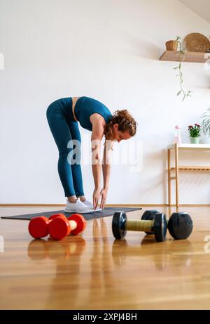 Caucasian young woman wearing sportswear doing fitness exercise at home. Active and healthy lifestyle. Stock Photo