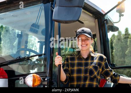 Portrait of woman wearing plaid shirt and cap next to the tractor. Stock Photo