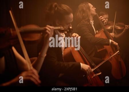 String quartet passionately playing cellos and violins while sitting in row on stage in misty orange light, copy space Stock Photo