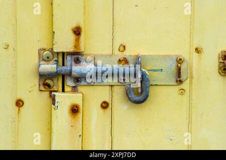 A metal bolt on a yellow painted wooden door with rusting nail heads Stock Photo