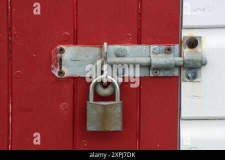 A metal bolt on a red door with brass padlock Stock Photo