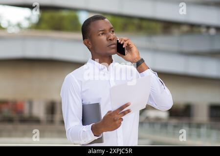 Young Man Engaged in a Phone Conversation While Holding Documents Stock Photo