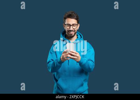 Young Man in Blue Hoodie Smiling While Using Smartphone Stock Photo