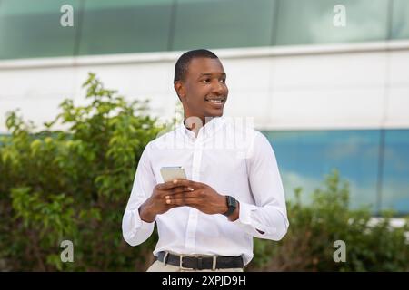 Young Man Smiling While Using Smartphone Near Modern Building Stock Photo