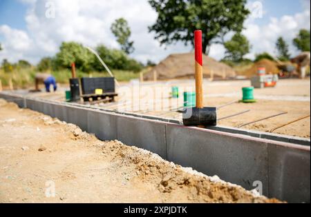 Close up of a rubber hammer standing on concrete curb stones, blurry background wit construction site workers  Stock Photo