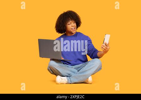 Young Man Sitting on Floor Using Laptop and Smartphone Stock Photo
